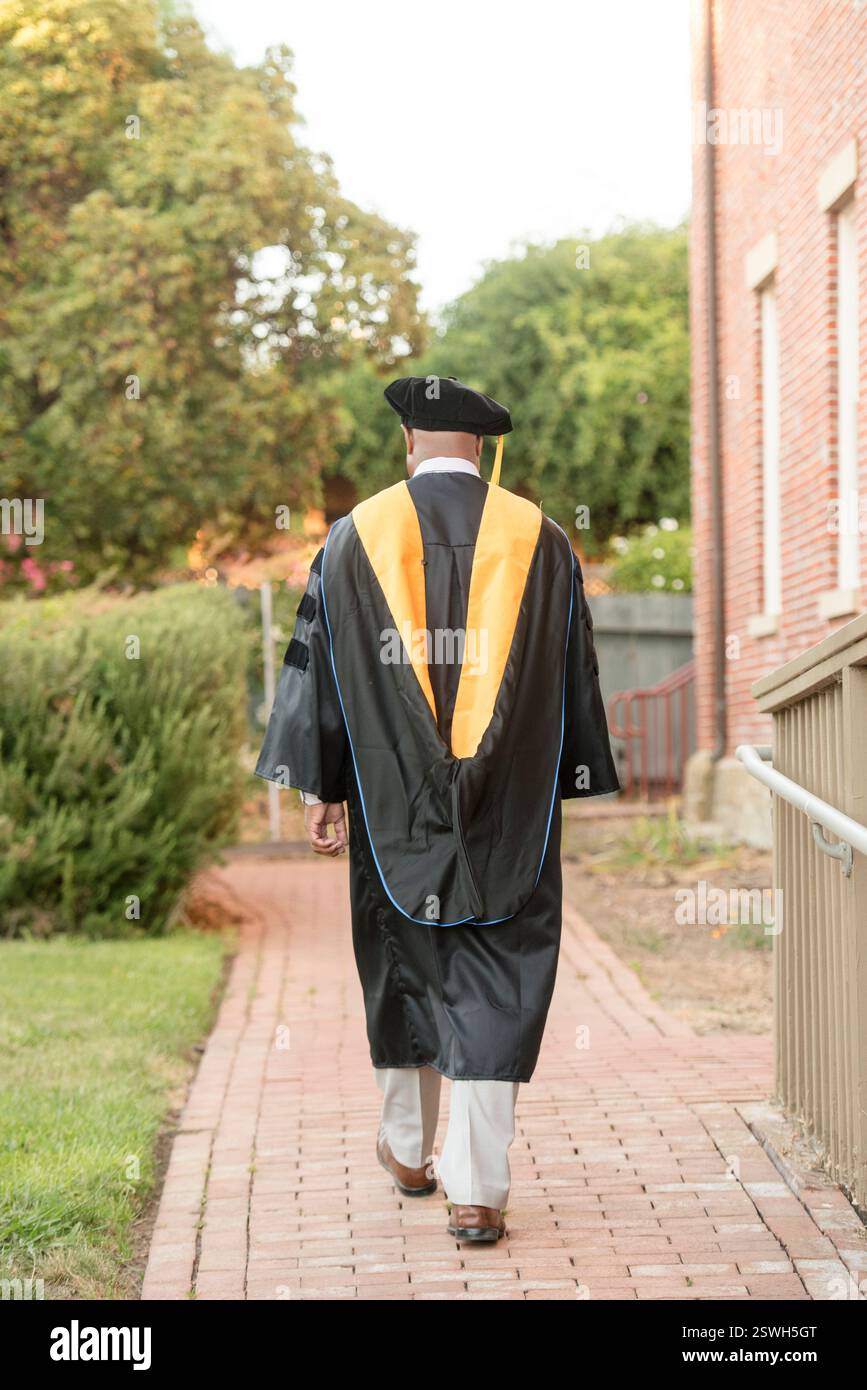 Abschluss in Promotionsregalia, die draußen auf einem Backsteinpfad laufen. Stockfoto