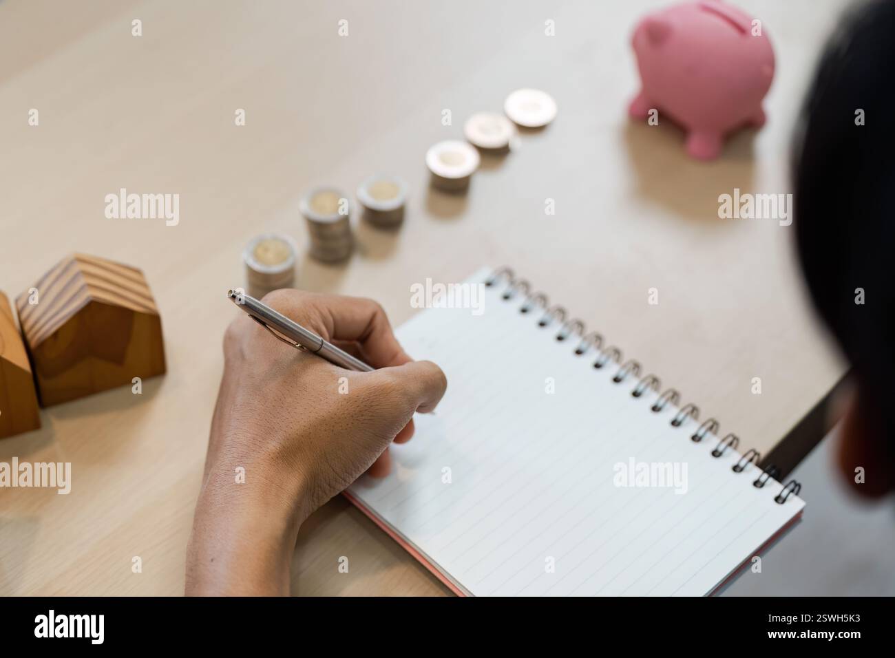 Individuelles Budgetieren und Sparen mit einem Notizbuch, Münzen und einer Sparkasse. Stockfoto
