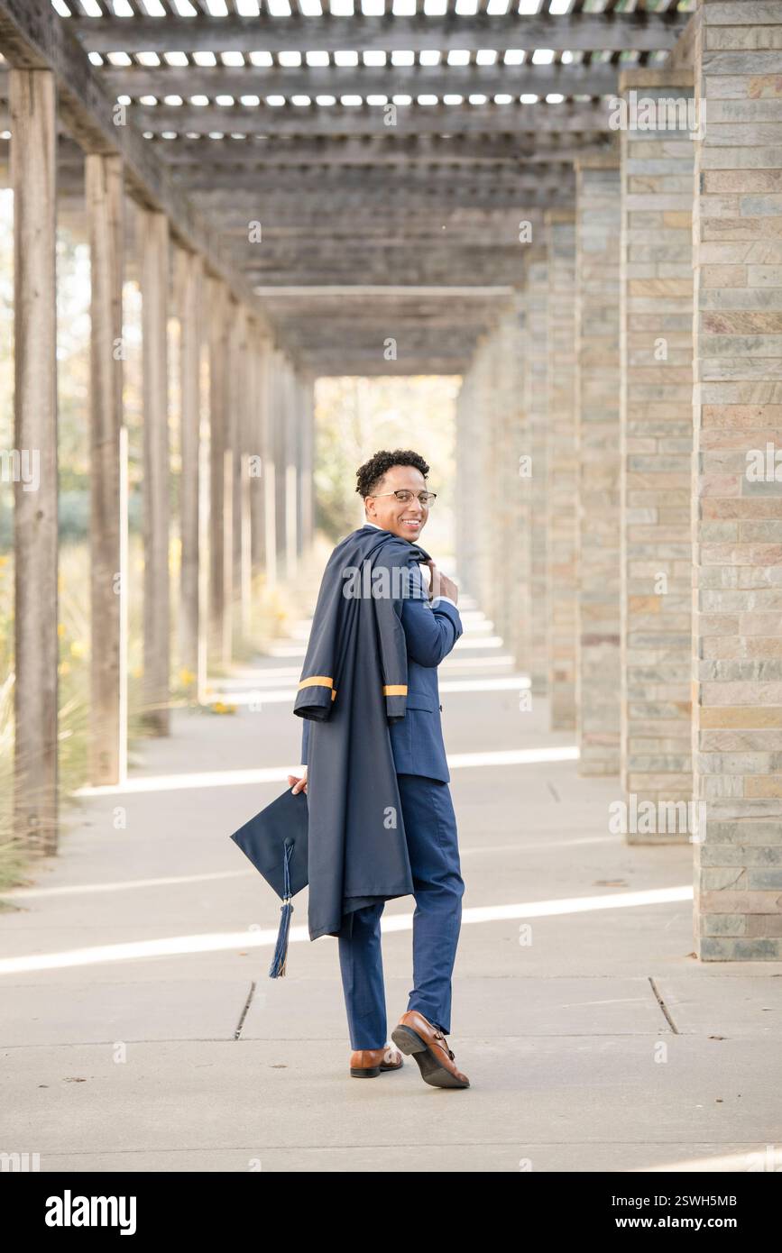 College-Absolvent geht weg und hält Mütze und Kleid Stockfoto