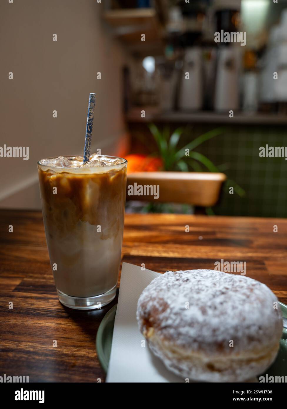Ein erfrischender Eiskaffee und ein gepuderter Donut auf einem hölzernen Kaffeetisch Stockfoto