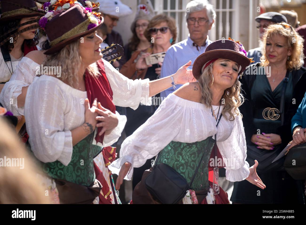 Das Bild zeigt zwei Personen in festlicher Kleidung mit weißen Blusen und dekorativen Hüten, die leidenschaftlich an einem Tanz oder einer Vorstellung beteiligt sind Stockfoto