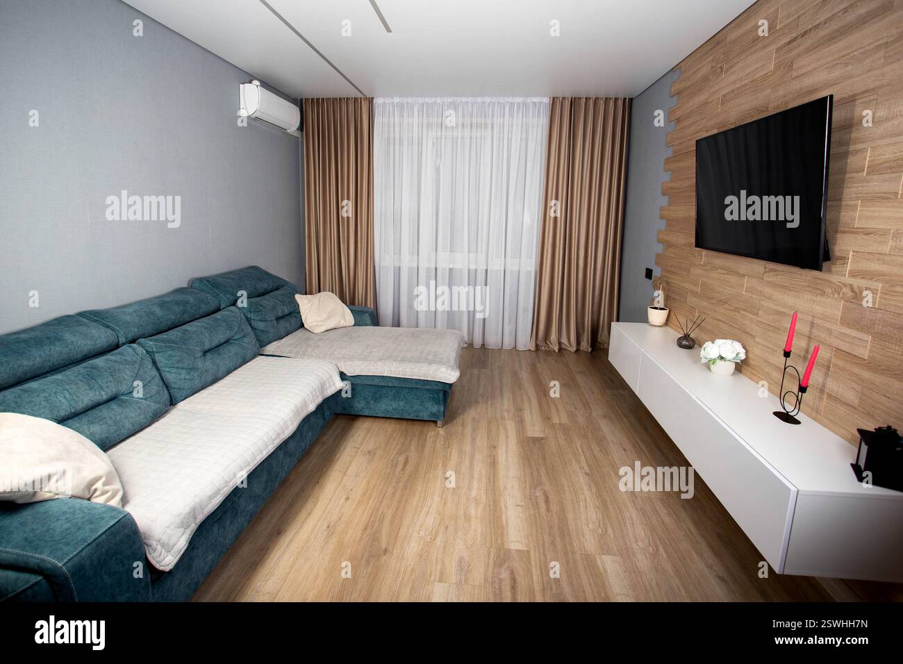 Modernes Wohnzimmer mit Laminatboden aus Holz, Wandschränken, LCD-Fernseher und Klimaanlage. Stilvolle Renovierung im Apartment Stockfoto