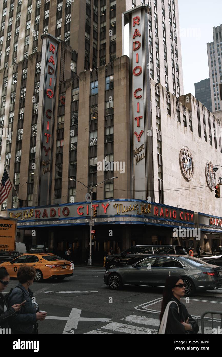 New York, USA - 8. April 2024: Eine lebendige Straßenszene in der Radio City Music Hall. Der legendäre Art déco-Veranstaltungsort, Neonlichter, Taxis und Fußgänger fangen ein Stockfoto