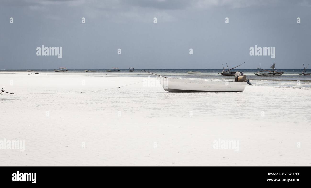 Weißes Fischerboot am Strand auf tropischem Hintergrund. Segelboote am Meer. Ebbe in der Lagune. Exotische Natur. Lokales nautisches Schiff in Afrika Stockfoto