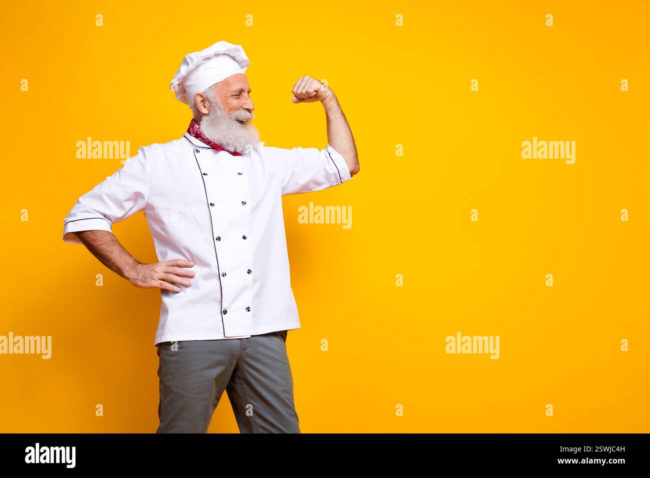 Chefkoch in Uniform, der seinen Arm selbstbewusst vor einem leuchtend gelben Hintergrund biegt Stockfoto