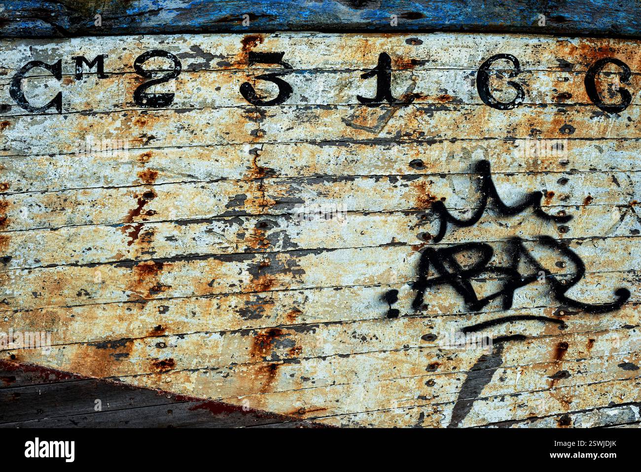 Le Fret, Halbinsel Crozon, Finistère, Bretagne, Frankreich: Schwarze Spraydosen-Graffiti auf dem abblätternden und rostgestreiften Rumpf eines verlassenen Fischerbootes stehen im Kontrast zu der typisch französischen Vintage-Schrift, die für die offizielle Zulassungsnummer und die abblätternde weiße Farbe auf dem Holzwerk verwendet wird. Stockfoto