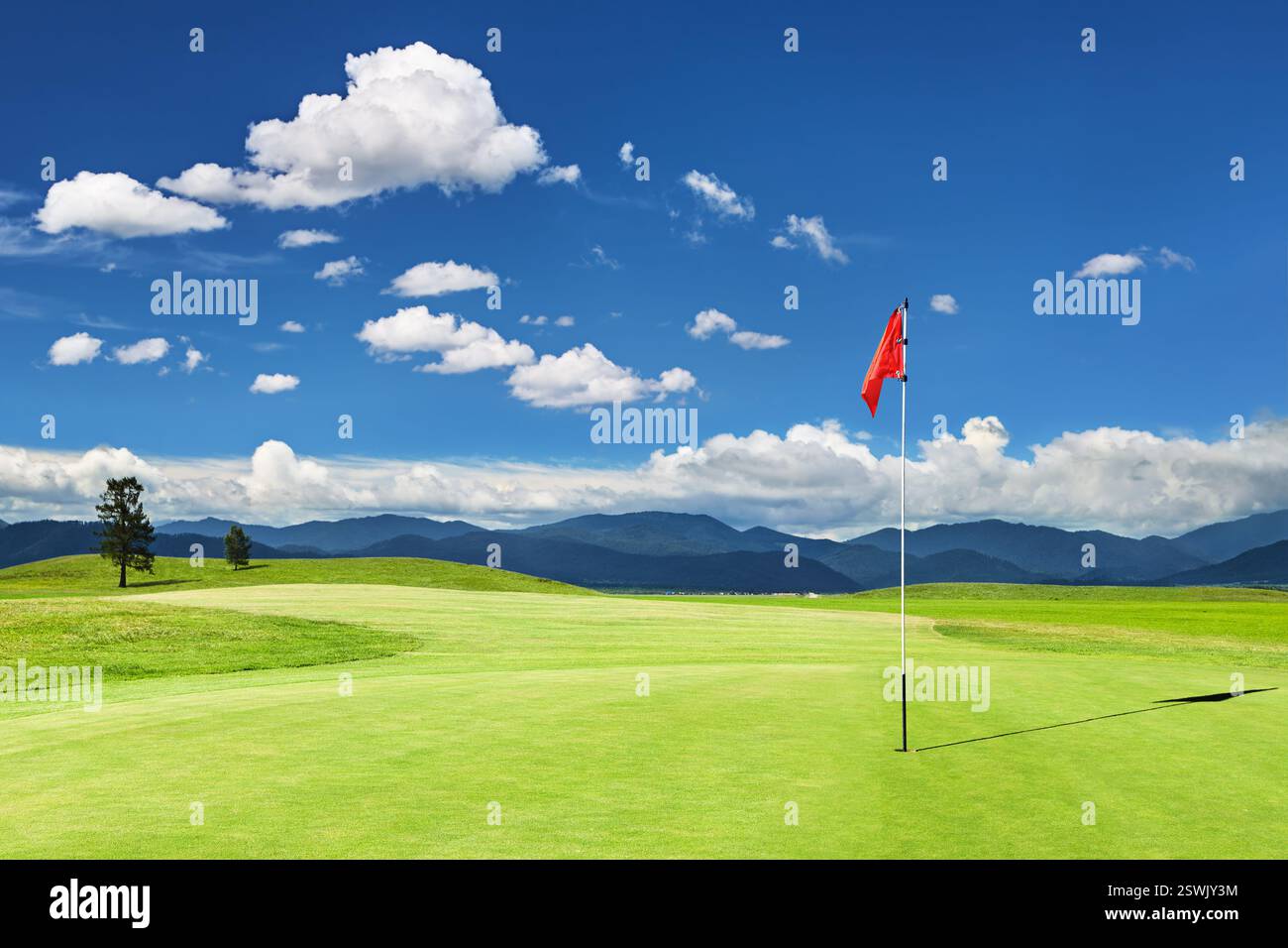 Schöner grüner Golfplatz mit Bergen, blauem Himmel und roter Flagge in einem Loch Stockfoto