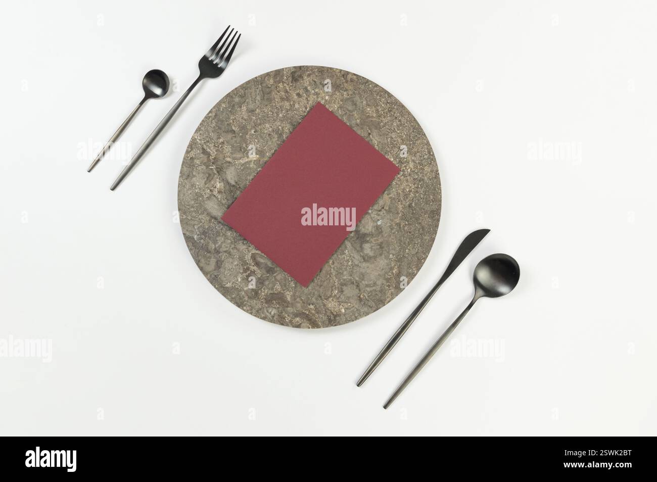 Blick von oben auf braunen Marmorteller, schwarzes Besteck und dunkelrote Karte auf weißem Hintergrund. Essenspräsentation, Steintablett. Tabelleneinstellung, Kopierbereich. Stockfoto Blick von oben auf braunen Marmorteller, schwarzes Besteck und dunkelrote Karte auf weißem Hintergrund. Essenspräsentation, Steintablett. Tabelleneinstellung, Kopierbereich. Stockfoto
