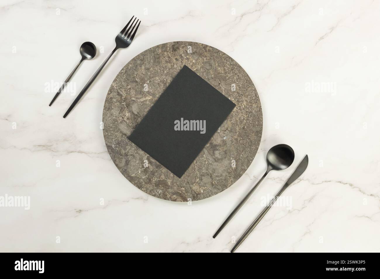 Blick von oben auf braunen Marmorteller, schwarzes Besteck und schwarze Karte auf weißem Marmorhintergrund. Essenspräsentation, Steintablett. Tabelleneinstellung, Kopierbereich. Stockfoto