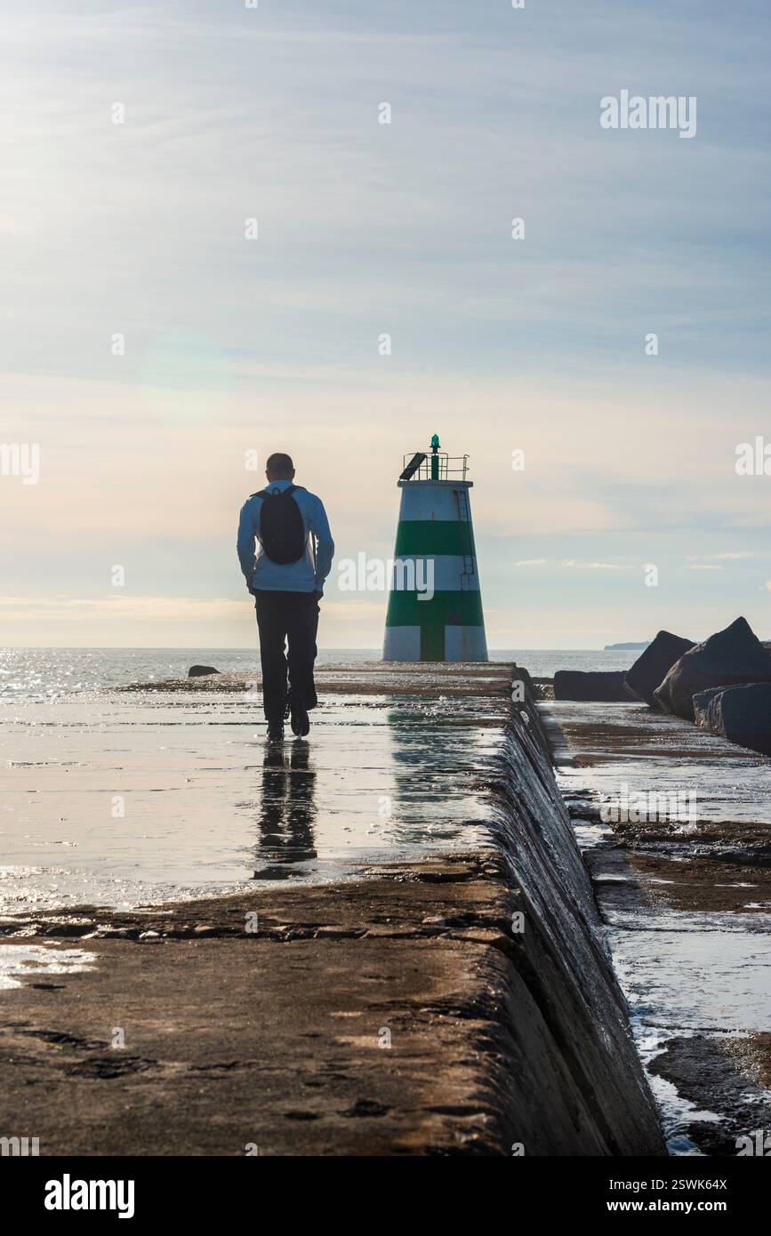 Mann, der zu einem Leuchtturm läuft, entlang eines Damms Stockfoto