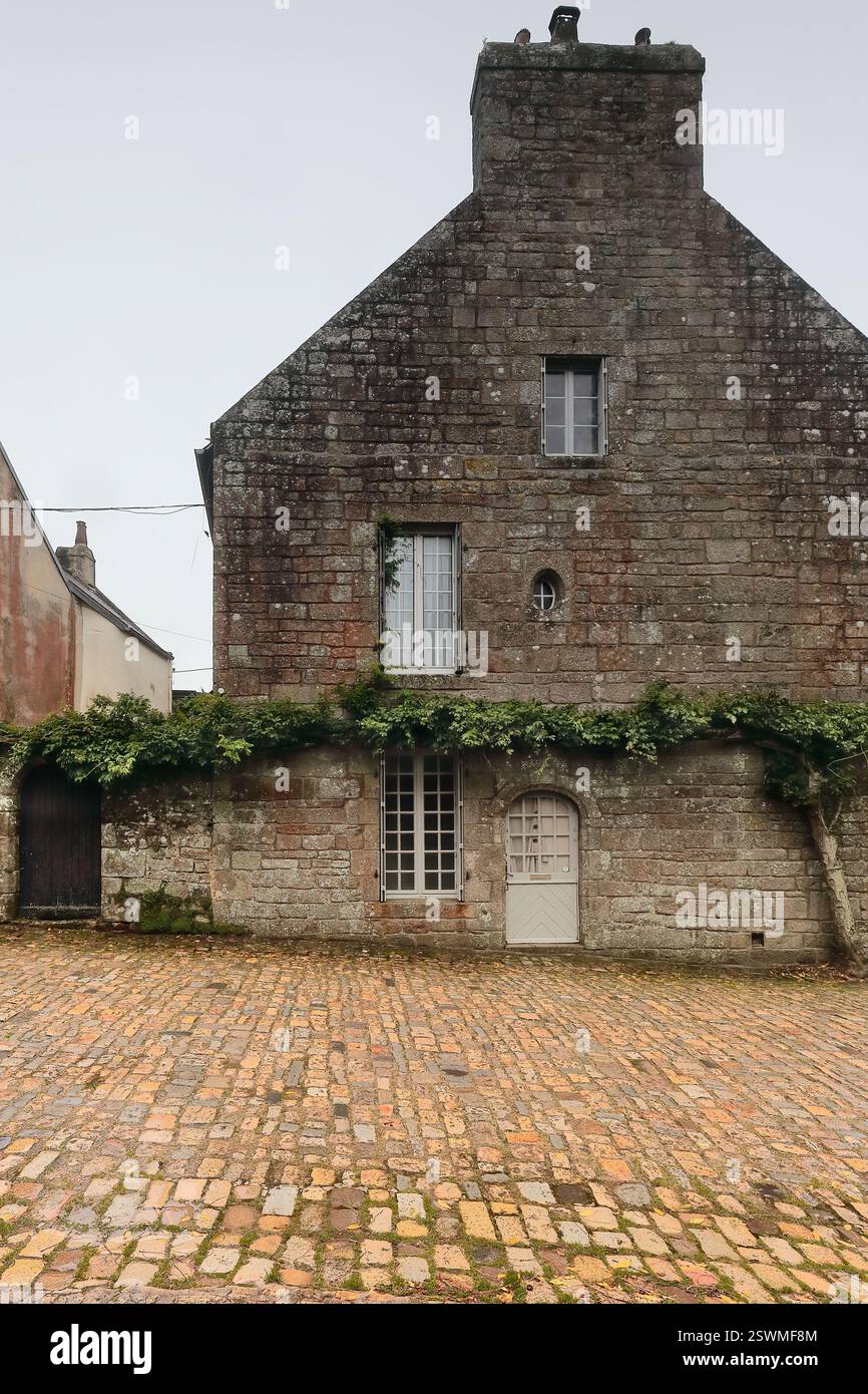 313 Granitfassade des Hauses auf der Westseite der Rue St.-Maurice Street, Ecke des Church Square, nicht blühende Glyzinien an der Wand. Locronan-Bretagne-Frankreich Stockfoto