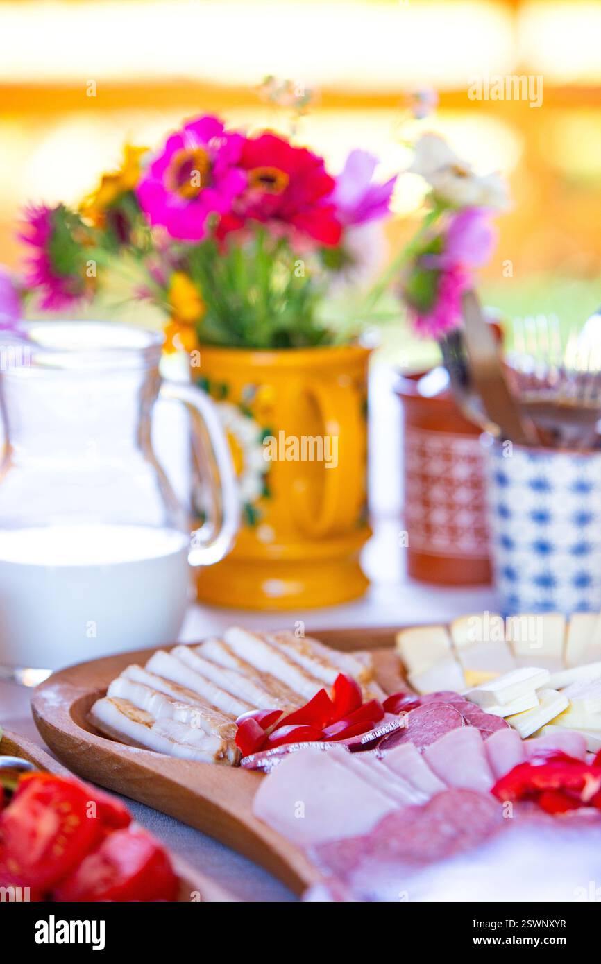Farbenfroher Frühstückstisch mit Käse, Gemüse und Blumen in natürlichem Licht. Stockfoto