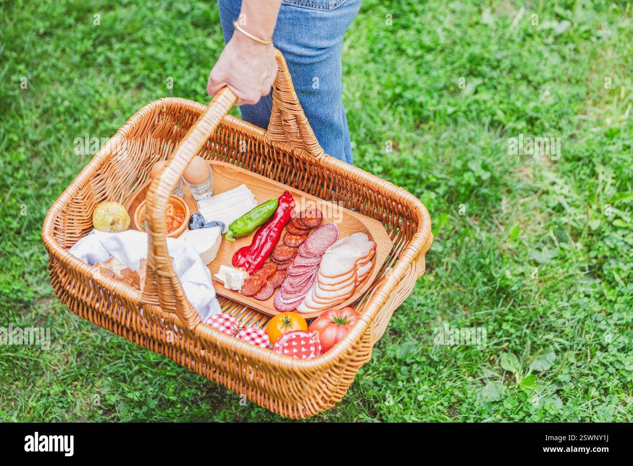 Nahaufnahme einer Hand, die einen gefüllten Picknickkorb im Freien trägt und köstliche Snacks präsentiert. Stockfoto