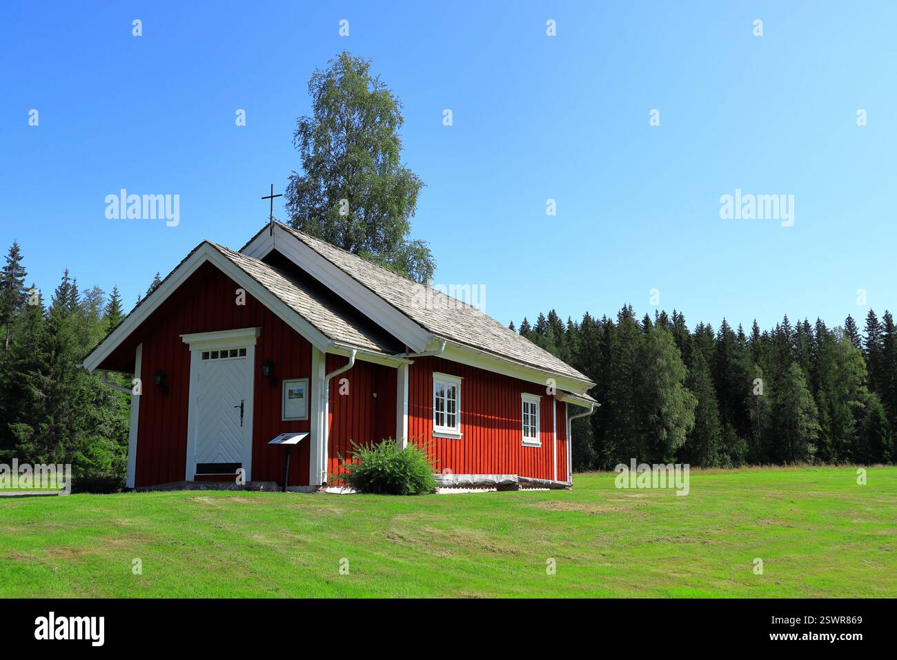 Eine winzige Kirche in einem idyllischen rot-weißen schwedischen Haus. Kleines Kreuz auf dem Dach. Toller Rasen ein sonniger Tag draußen. Wald und blauer Himmel. Värmland, Swed Stockfoto