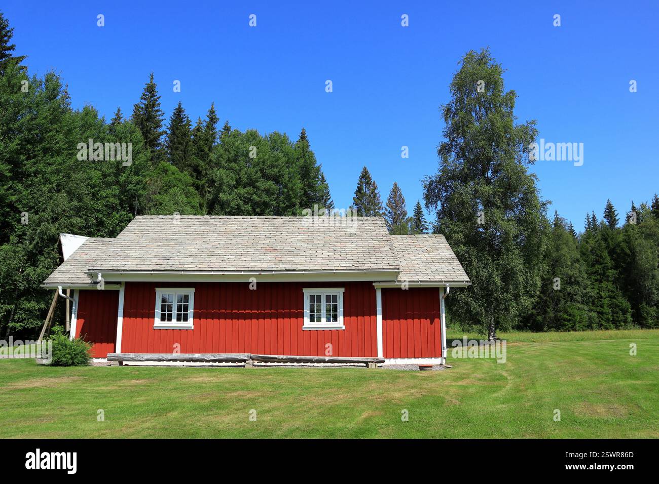 Eine winzige Kirche in einem idyllischen rot-weißen schwedischen Haus. Kleines Kreuz auf dem Dach. Toller Rasen ein sonniger Tag draußen. Wald und blauer Himmel. Värmland, Swed Stockfoto