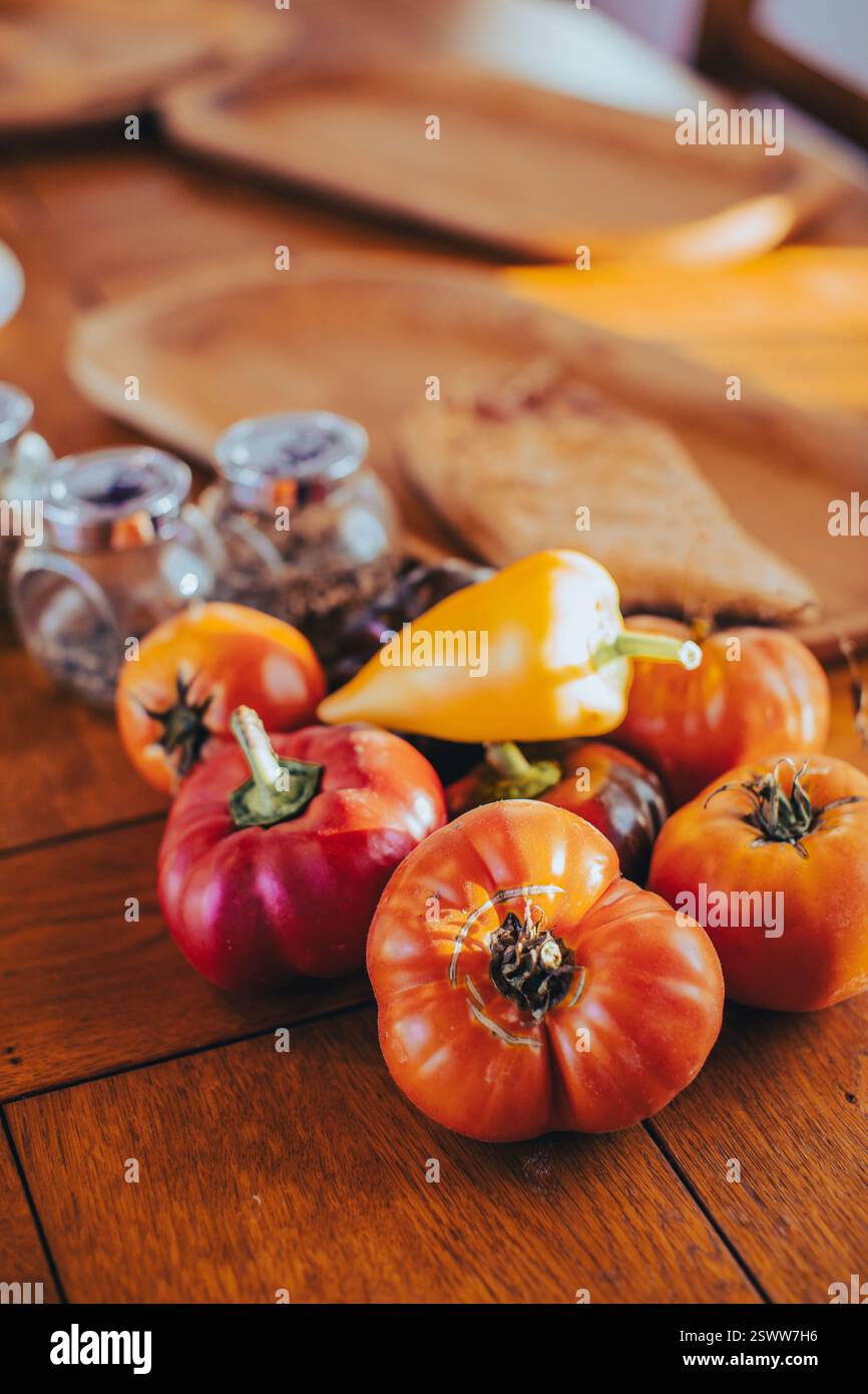 Verschiedene lebendige Tomaten und Paprika auf einem Holztisch in warmer Beleuchtung. Stockfoto