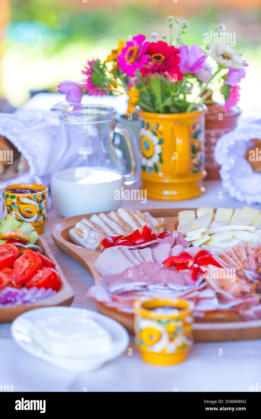 Ein lebhafter Frühstückstisch mit Blumen, Speisen und Getränken im Freien. Stockfoto
