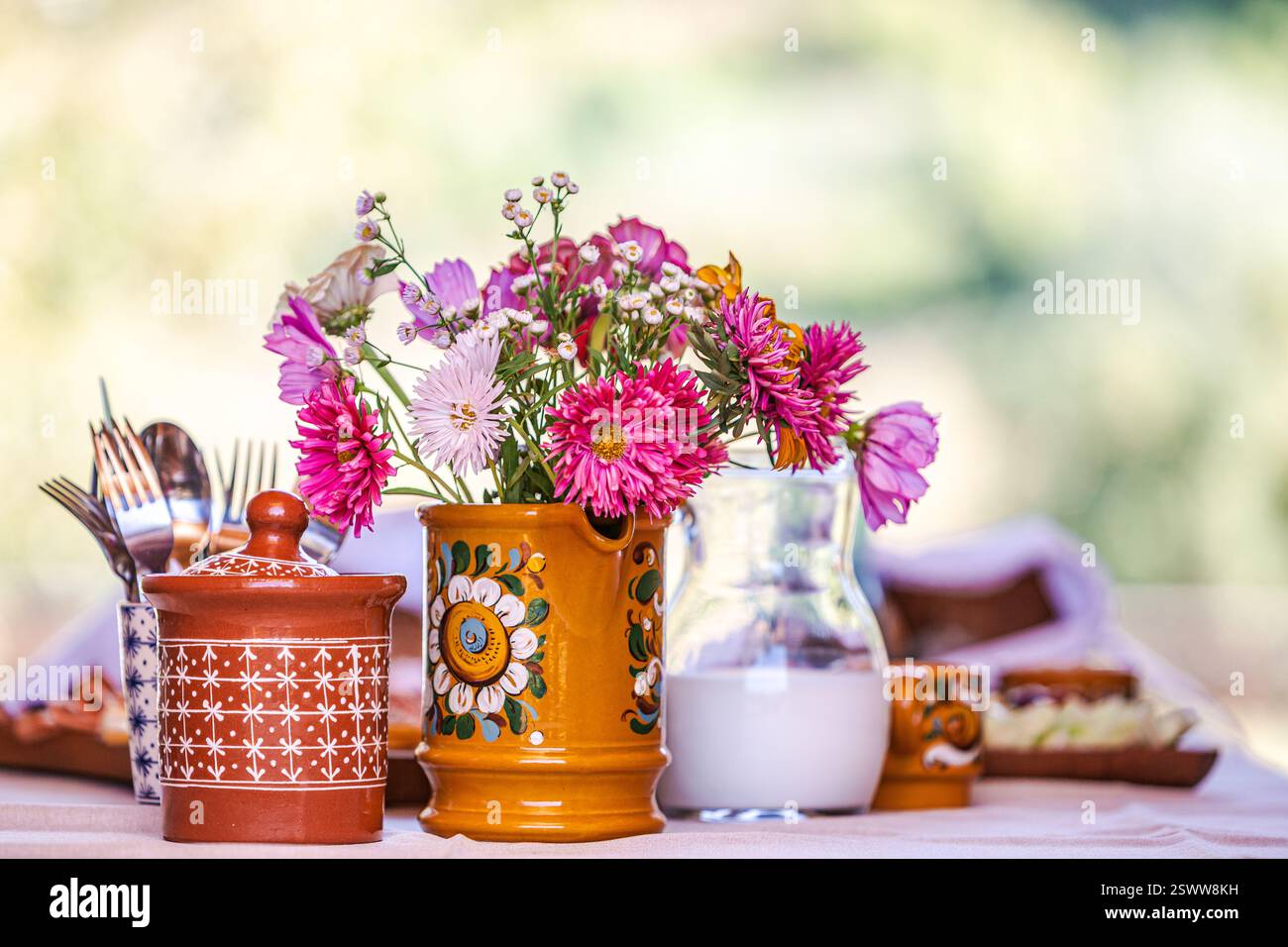 Bunte Blumen in Keramikvase auf einem sonnigen Tisch mit traditioneller Keramik. Stockfoto