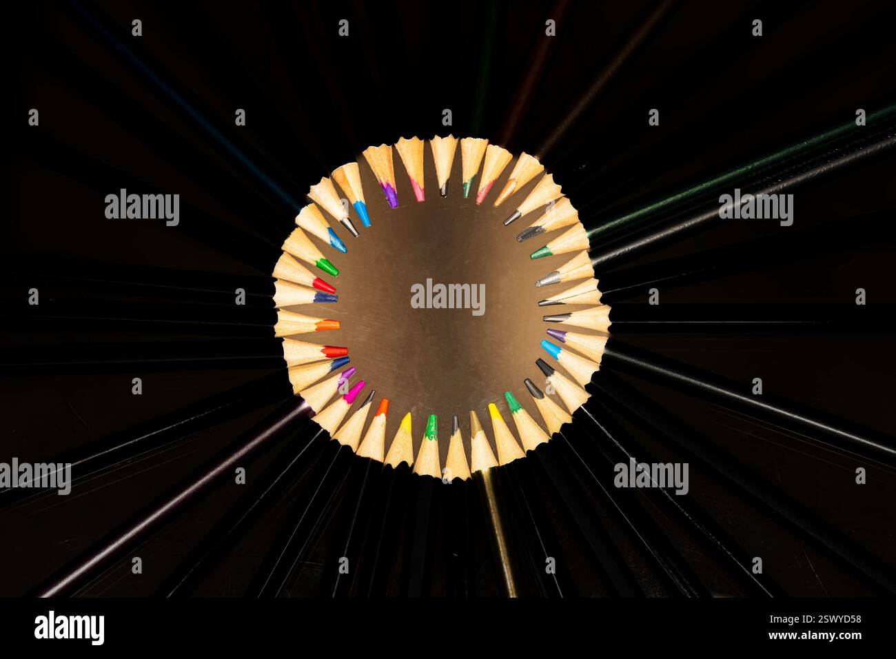 Radiale Anordnung von schwarzen Bleistiften mit freiliegenden bunten Spitzen, die eine kreisförmige Komposition vor dunklem Hintergrund bilden Stockfoto