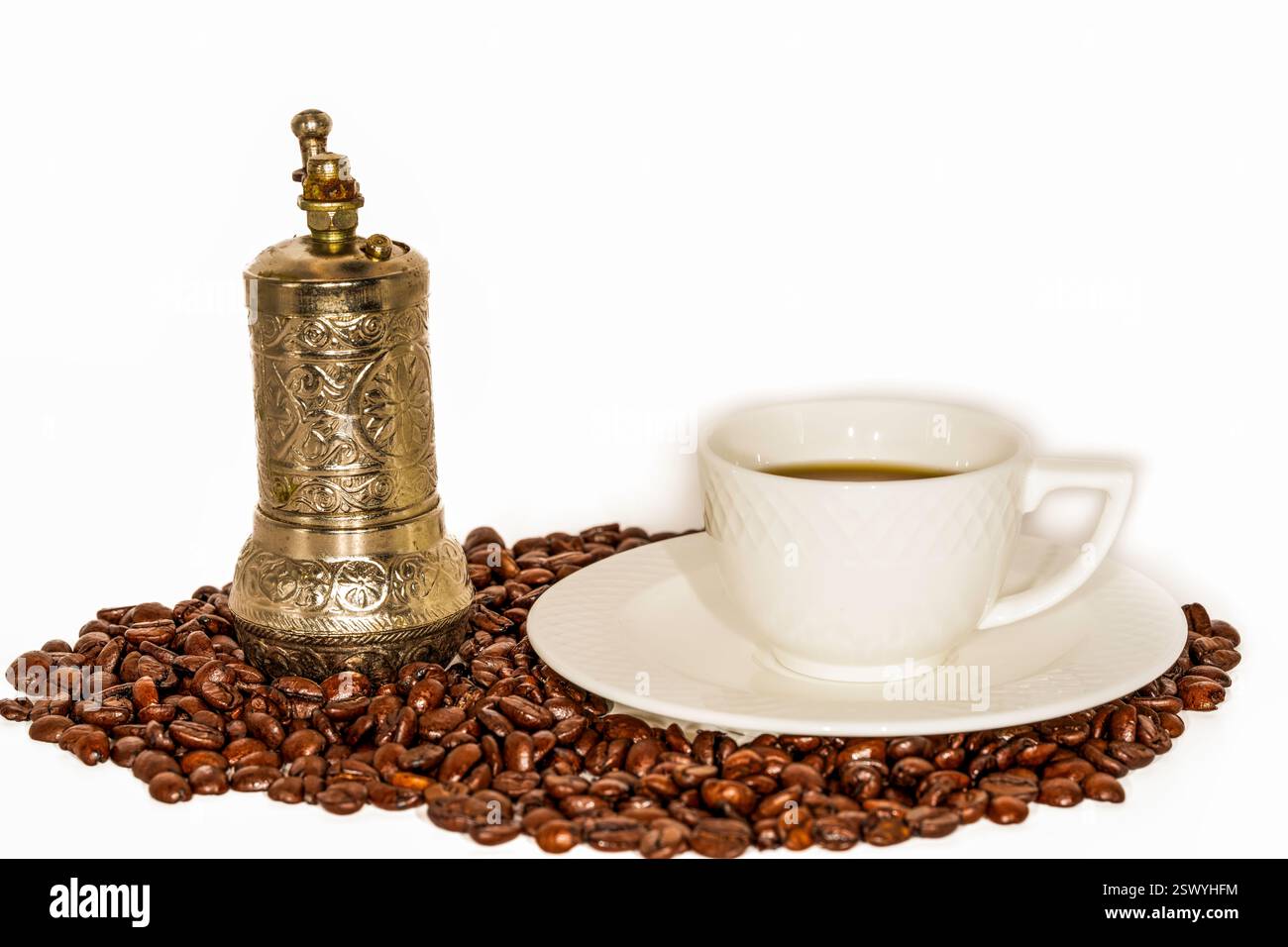 Vintage-Handkaffeemühle mit kunstvollem Metalldesign und klassischer weißer Kaffeetasse auf einer Untertasse, umgeben von gerösteten Kaffeebohnen Stockfoto