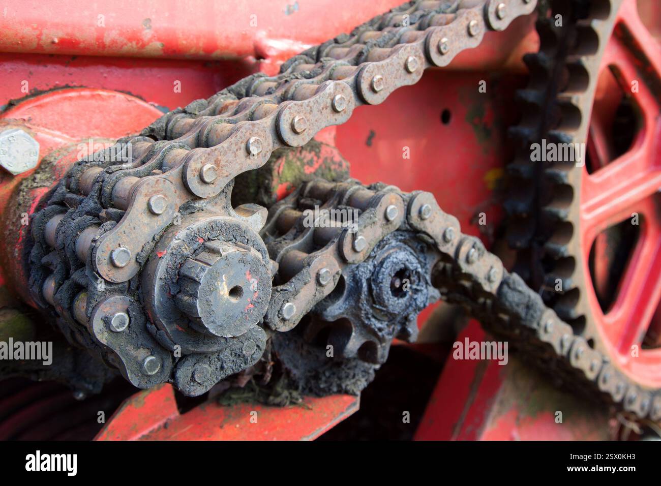 Ein stark verschmutzter Kettenantrieb mit Zahnrädern, die mit Schmutz, Rost an der Kette und altem schwarzem Fett bedeckt sind, ein auffälliges Bild von vernachlässigter Wartung. Stockfoto