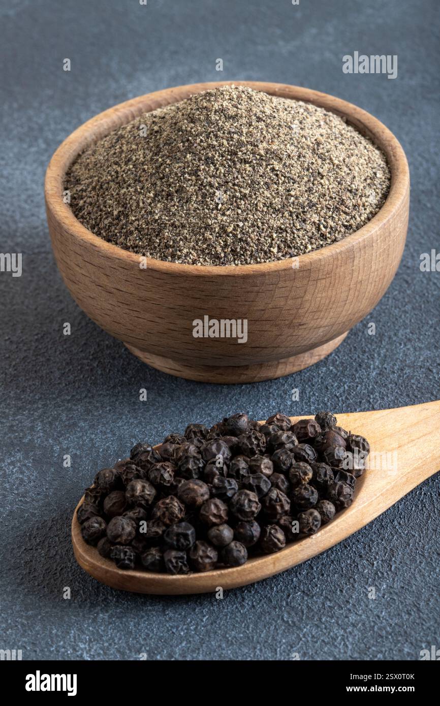 Gemahlener schwarzer Pfeffer mit Körnern schwarzen Pfeffers auf grauem Hintergrund Stockfoto