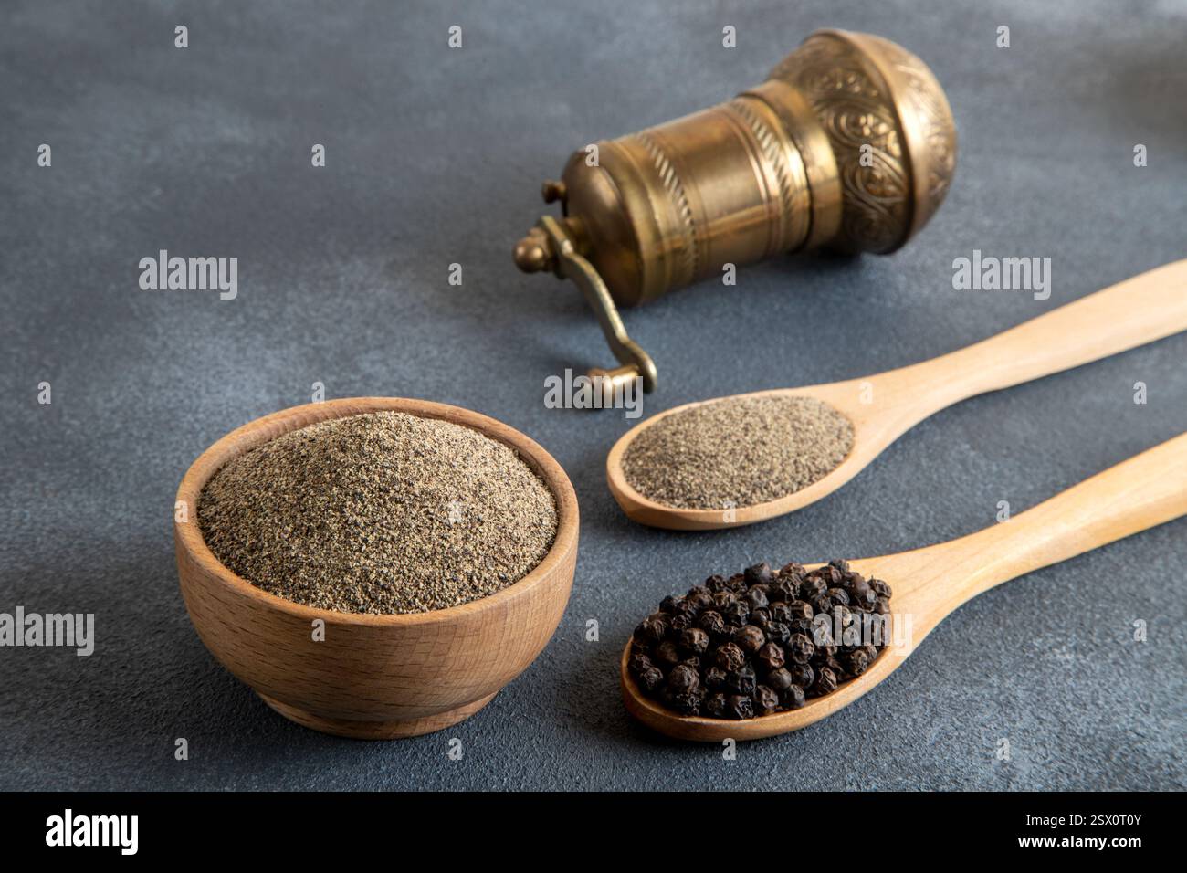 Schüsseln mit schwarzen Pfefferkörnern auf schwarzem Hintergrund und eine Metallschleifmaschine Stockfoto