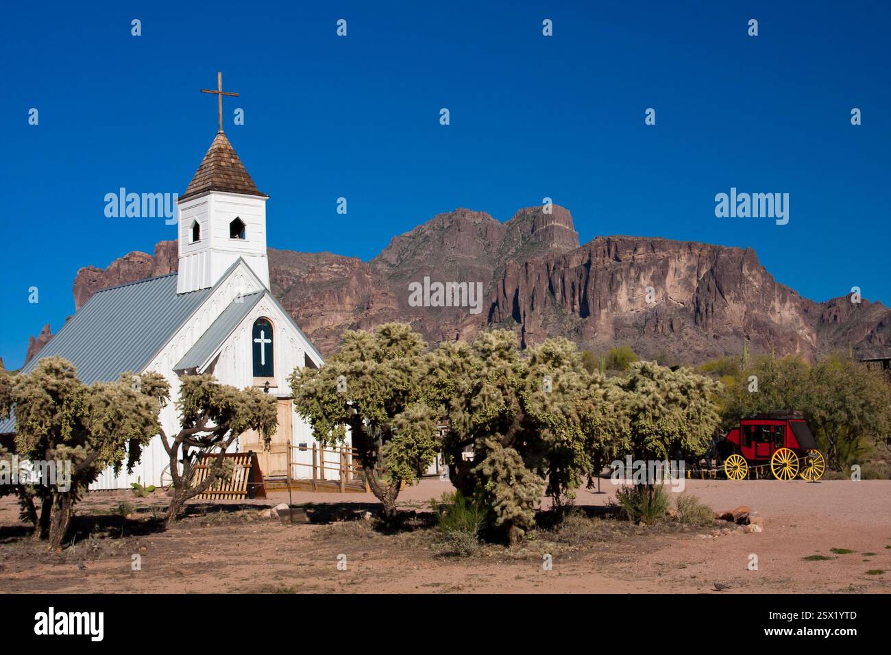 Eine kleine weiße Kirche mit einem Kreuz auf der Spitze steht vor einem großen Berg. Die Kirche ist von Bäumen umgeben und davor steht eine Kutsche. T Stockfoto