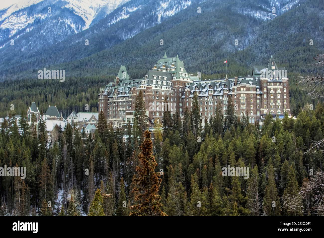 Großes Hotel mit einem Berg im Hintergrund. Das Hotel ist von Bäumen und Schnee umgeben. Das Konzept von Luxus und Ruhe, da das Hotel in A eingebettet ist Stockfoto