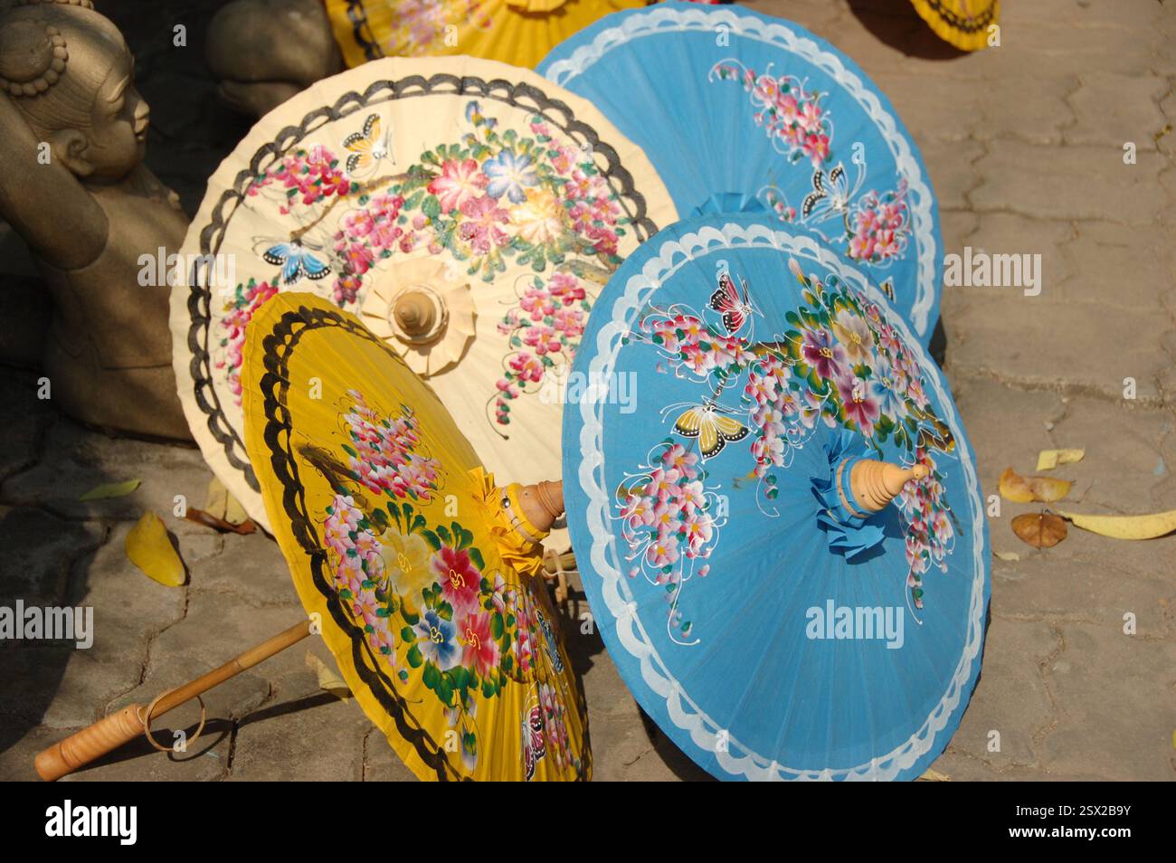 Handgefertigte Regenschirme aus Holz und Bambuspapier mit traditionellen thailändischen Blumenmustern, in lebhaften Farben bemalt, auf dem Boden unter der Sonne Stockfoto