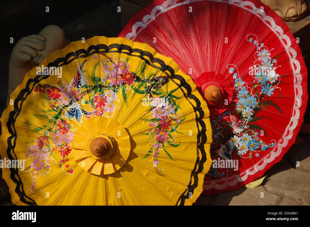 Handgefertigte Regenschirme aus Holz und Bambuspapier mit traditionellen thailändischen Blumenmustern, in lebhaften Farben bemalt, auf dem Boden unter der Sonne Stockfoto