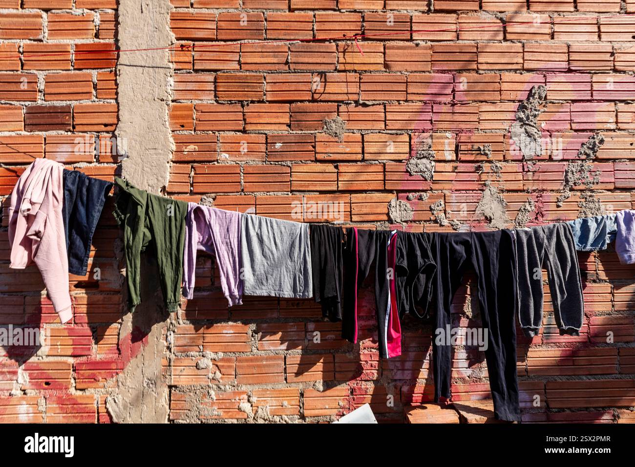 Detail der Kleidung, die auf einer Wäscheleine an einer Backsteinmauer gewaschen wurde, in der armen Nachbarschaft von Diadema, Randstadt von São Paulo, Brasilien Stockfoto