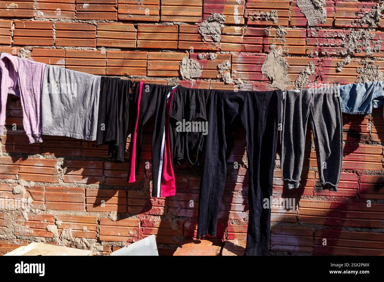 Detail der Kleidung, die auf einer Wäscheleine an einer Backsteinmauer gewaschen wurde, in der armen Nachbarschaft von Diadema, Randstadt von São Paulo, Brasilien Stockfoto