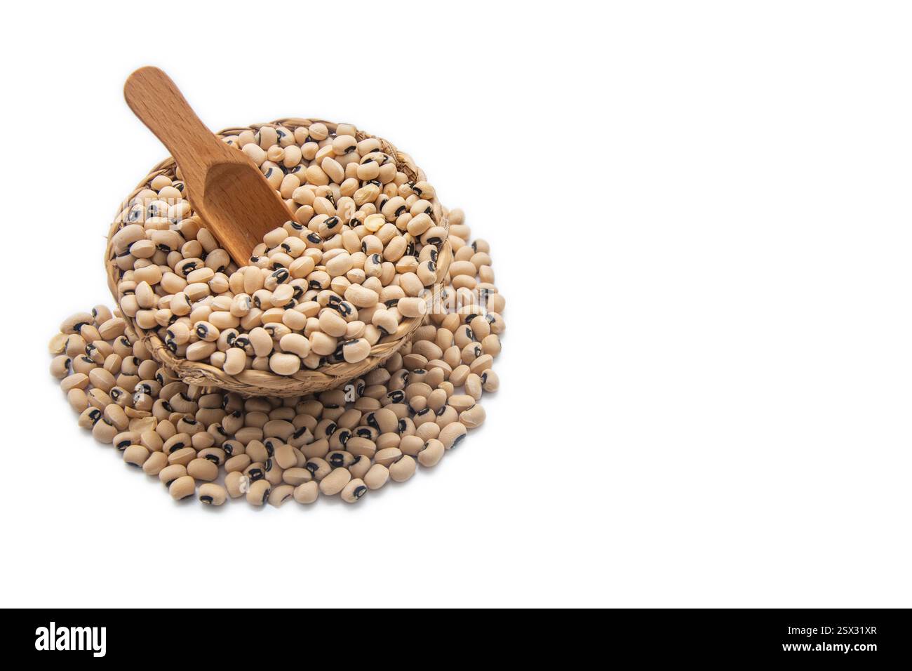 Eine Korbschale gefüllt mit schwarzäugigen Erbsen, mit einem Holzlöffel innen und umgeben von verstreuten schwarzäugigen Erbsen. Stockfoto