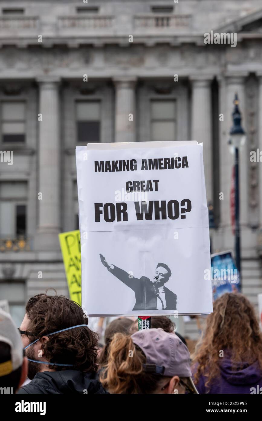 San Francisco, Kalifornien, USA, 17. Februar 2025. Demonstranten versammeln sich vor dem Rathaus von San Francisco, um gegen die jüngsten Aktionen von Präsident Donald Trump und Elon Musk zu protestieren, darunter das Einfrieren von Bundesgeldern, die Entlassung von Bundesarbeitern und die Einwanderungspolitik. Über der Menge steht ein Schild: "Amerika für wen großartig machen?" Mit einem Foto von Elon Musk, das aussieht wie ein nazi, der einen Gruß gibt. Quelle: Shelly Rivoli/Alamy Stockfoto