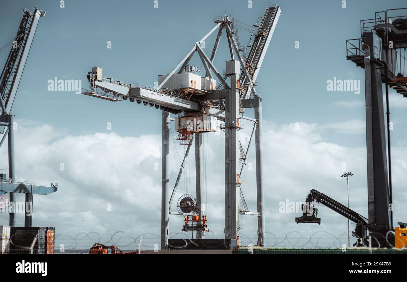 Teleaufnahme eines großen Industriekontainerkrans in einem belebten Schiffshafen. Robuste Stahlkonstruktion mit mechanischen Armen, Steuerkabine und Zugvorrichtung Stockfoto