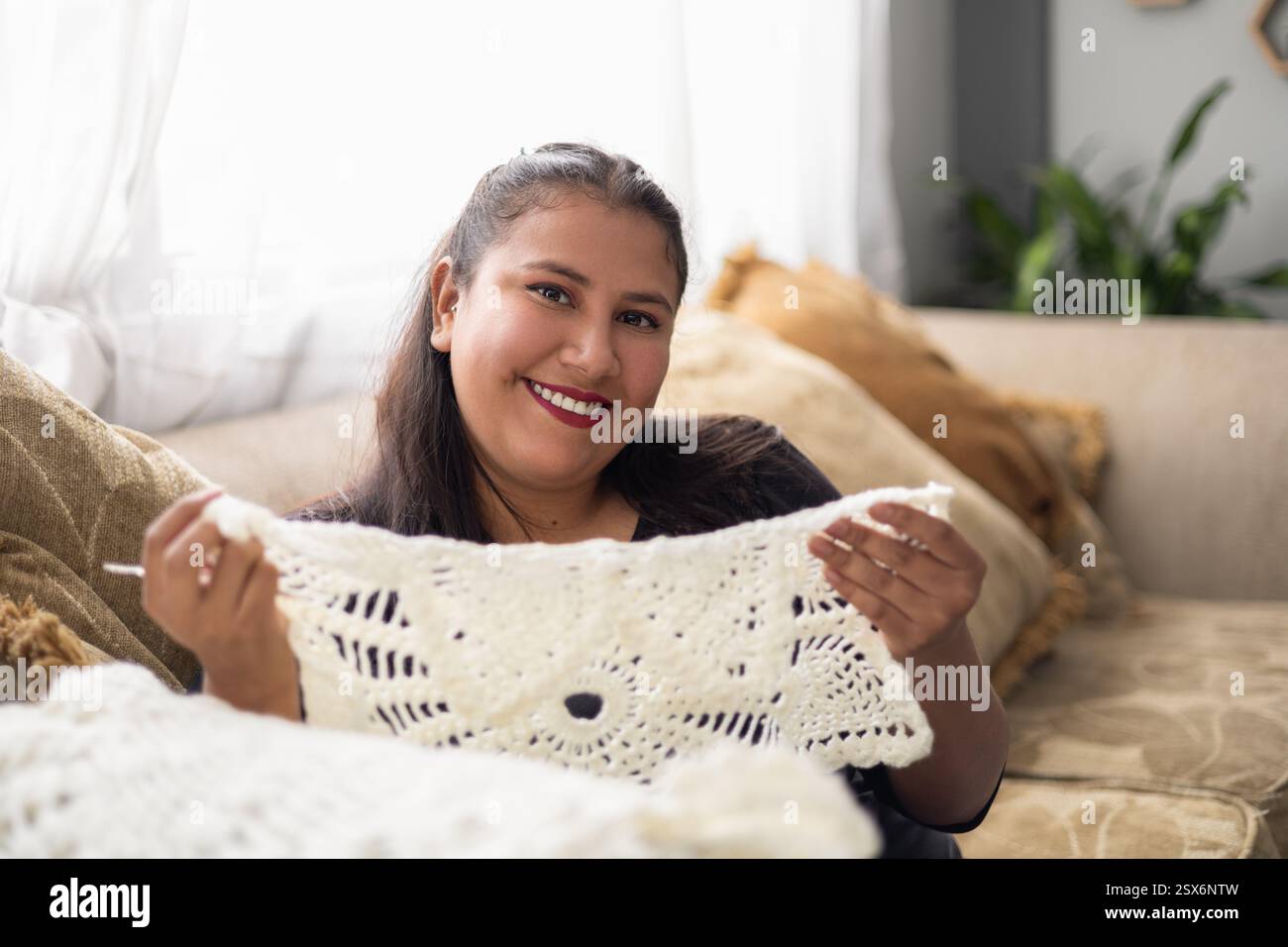 Eine lächelnde Latina-Frau zeigt stolz ihren handgefertigten Teppich, perfekt für Inhalte über Kunsthandwerk, handgefertigte Gegenstände und Wohnkultur. Stockfoto
