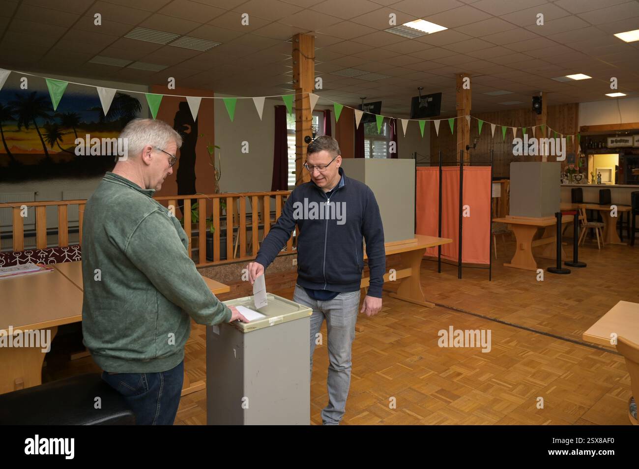 Wolferode, Deutschland. Februar 2025. Carsten Zeugner gibt seinen Wahlzettel in der Wahlurne des Wahlhauses Wolferode ab, während Peter Kößler vom Wahlausschuss den Prozess aufmerksam beobachtet. Die Wahlstation befindet sich im Restaurant „zum Anker“. Die Vorwahl zum 21. Deutschen Bundestag findet am Sonntag statt. Quelle: Heiko Rebsch/dpa/Alamy Live News Stockfoto