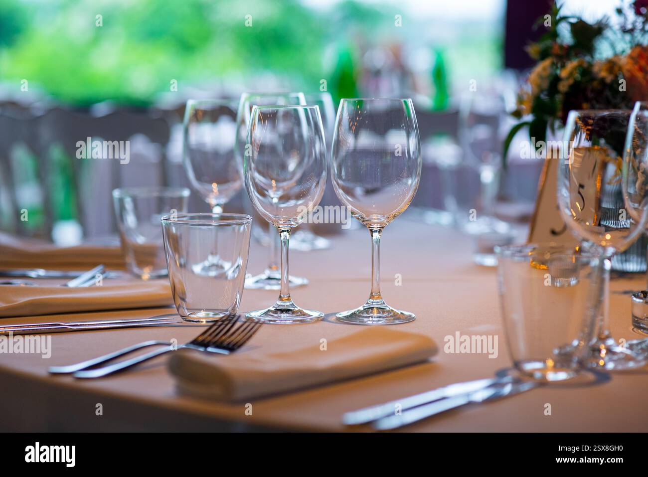 Ein wunderschön gestalteter Tisch mit glänzenden Gläsern und poliertem Besteck, umgeben von üppigem Grün und hellem Sonnenlicht, sorgt für einen perfekten Amb Stockfoto