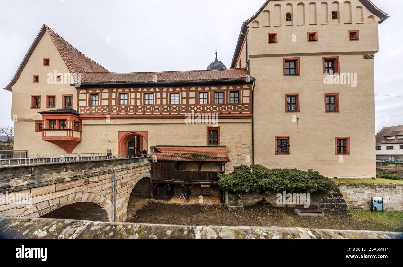 Ein asphaltierter Fußweg führt zur Kaiserpfalz in Forchheim und zeigt ein historisches Gebäude mit dekorativen Fachwerkelementen und gemeißelten Elementen. Ein Steinrelief und Säulen sind sichtbar. Forchheim, Bayern, Deutschland Eine Steinbrücke überspannt einen Innenhof vor einem historischen Schloss in Deutschland Menschen sind auf der Brücke zu sehen. Stockfoto
