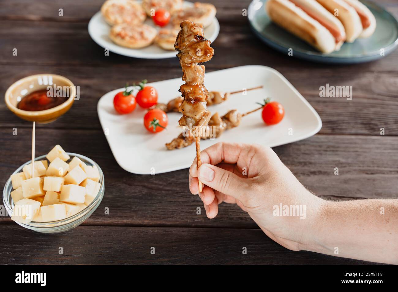 Eine Hand hält einen gegrillten Hähnchenspieß mit Barvorspeisen auf einem Holztisch Stockfoto