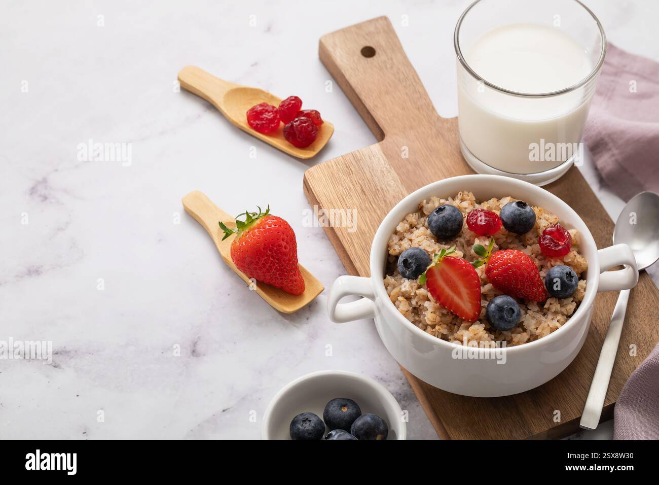 Buchweizenflocken mit Erdbeeren und Heidelbeeren in keramischer weißer Platte auf Holztablett mit Kopierraum Stockfoto