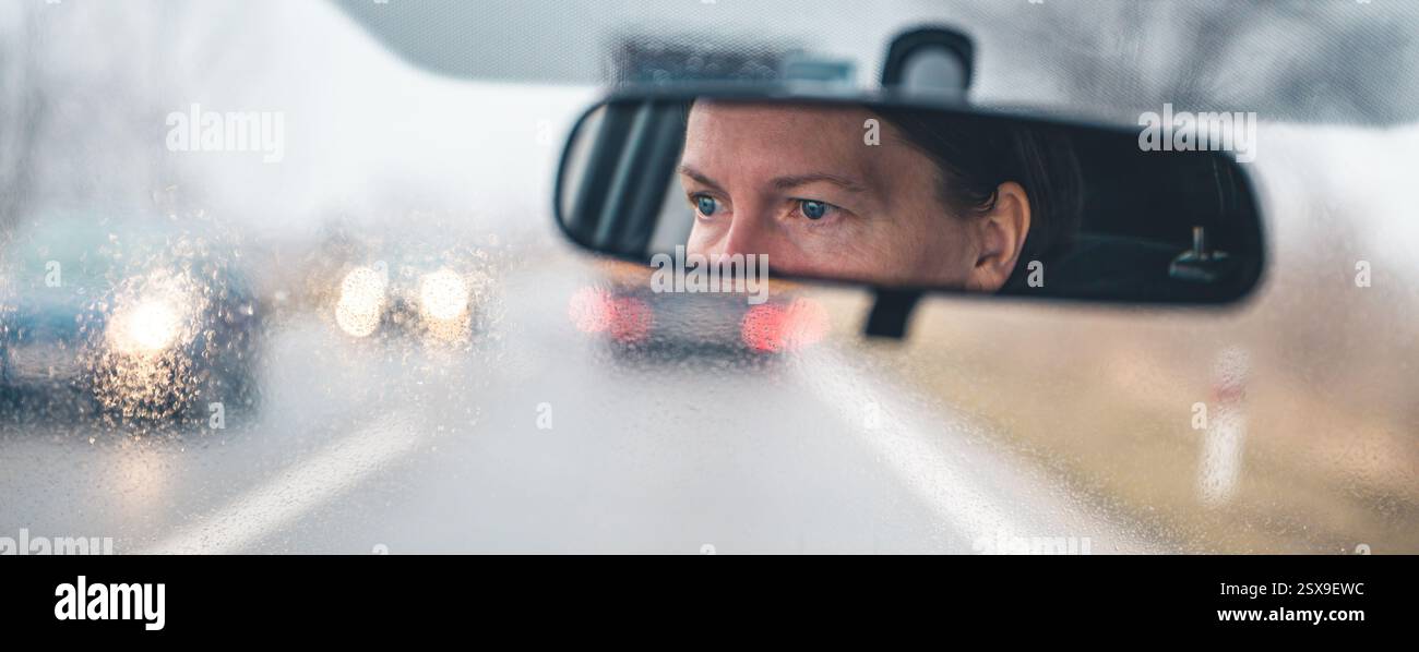 Weibliches Fahrergesicht am Rückspiegel an einem regnerischen Tag, selektiver Fokus Stockfoto
