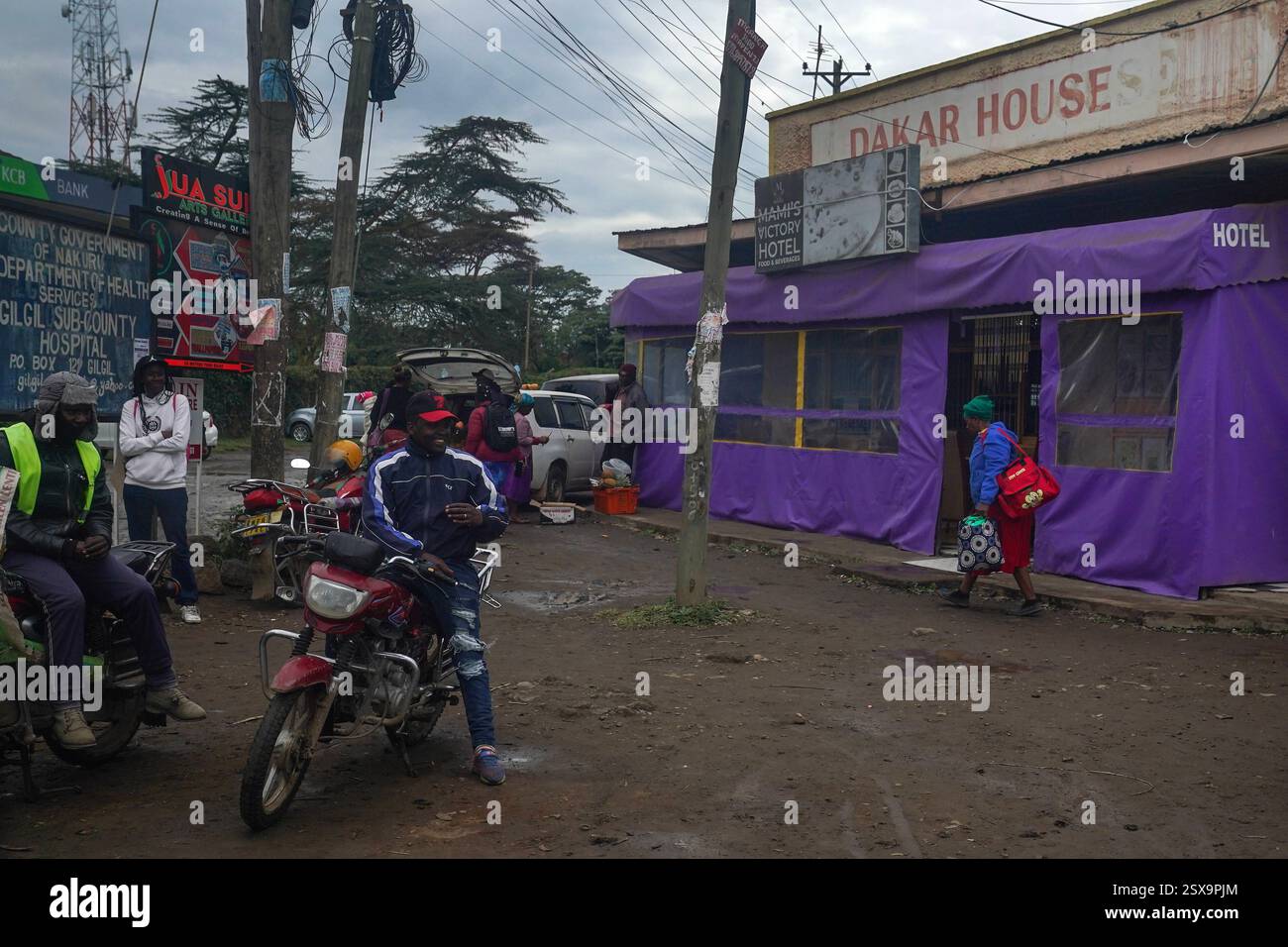 Das tägliche Leben in Gilgil, Kenia Männer ruhen sich am 30. Januar 2025 auf geparkten Motorrädern vor dem Mamis Victory Hotel in Gilgil, Kenia aus. Gilgil ist eine kleine, aber lebendige Stadt im Nakuru County, Kenia, am Rande des Great Rift Valley. Gilgil ist traditionell für seine landwirtschaftlichen Wurzeln bekannt und hat sich zunehmend zu einem Drehkreuz für Kleinunternehmen entwickelt, was die umfassenderen wirtschaftlichen Veränderungen in Kenia widerspiegelt. Lokale Unternehmer nutzen die robuste Telekommunikationsinfrastruktur der Nationen, die für Innovationen wie mobile Gelddienste bekannt ist, um sich mit breiteren Märkten zu verbinden und den Betrieb zu optimieren. Dies Stockfoto