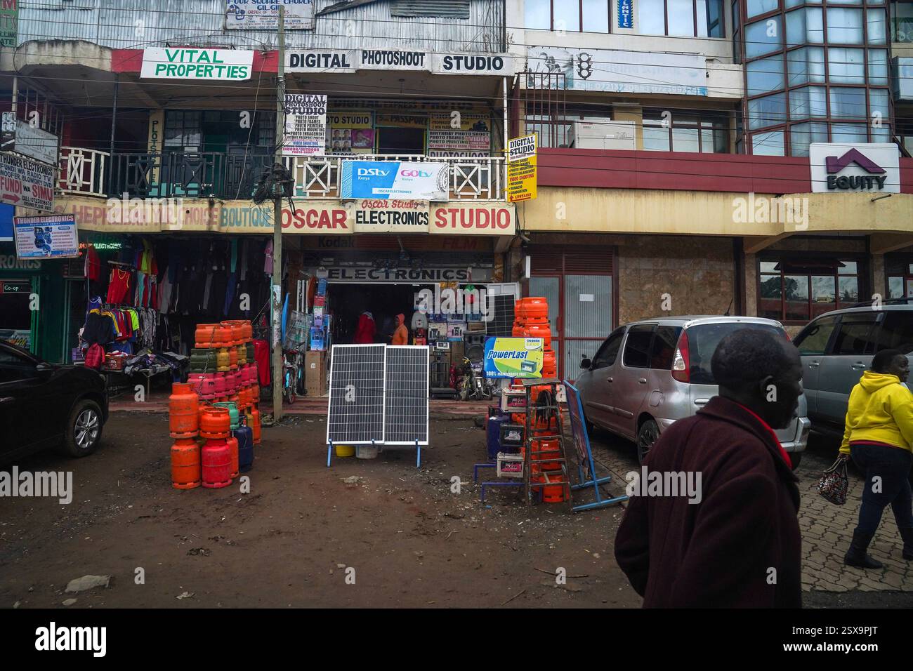 Das tägliche Leben in Gilgil, Kenia, läuft am 30. Januar 2025 Ein Mann an einem Elektronikgeschäft vorbei, das Solarpaneele und LP-Gasflaschen verkauft. Gilgil ist eine kleine, aber lebendige Stadt im Nakuru County, Kenia, am Rande des Great Rift Valley. Gilgil ist traditionell für seine landwirtschaftlichen Wurzeln bekannt und hat sich zunehmend zu einem Drehkreuz für Kleinunternehmen entwickelt, was die umfassenderen wirtschaftlichen Veränderungen in Kenia widerspiegelt. Lokale Unternehmer nutzen die robuste Telekommunikationsinfrastruktur der Nationen, die für Innovationen wie mobile Gelddienste bekannt ist, um sich mit breiteren Märkten zu verbinden und zu rationalisieren Stockfoto