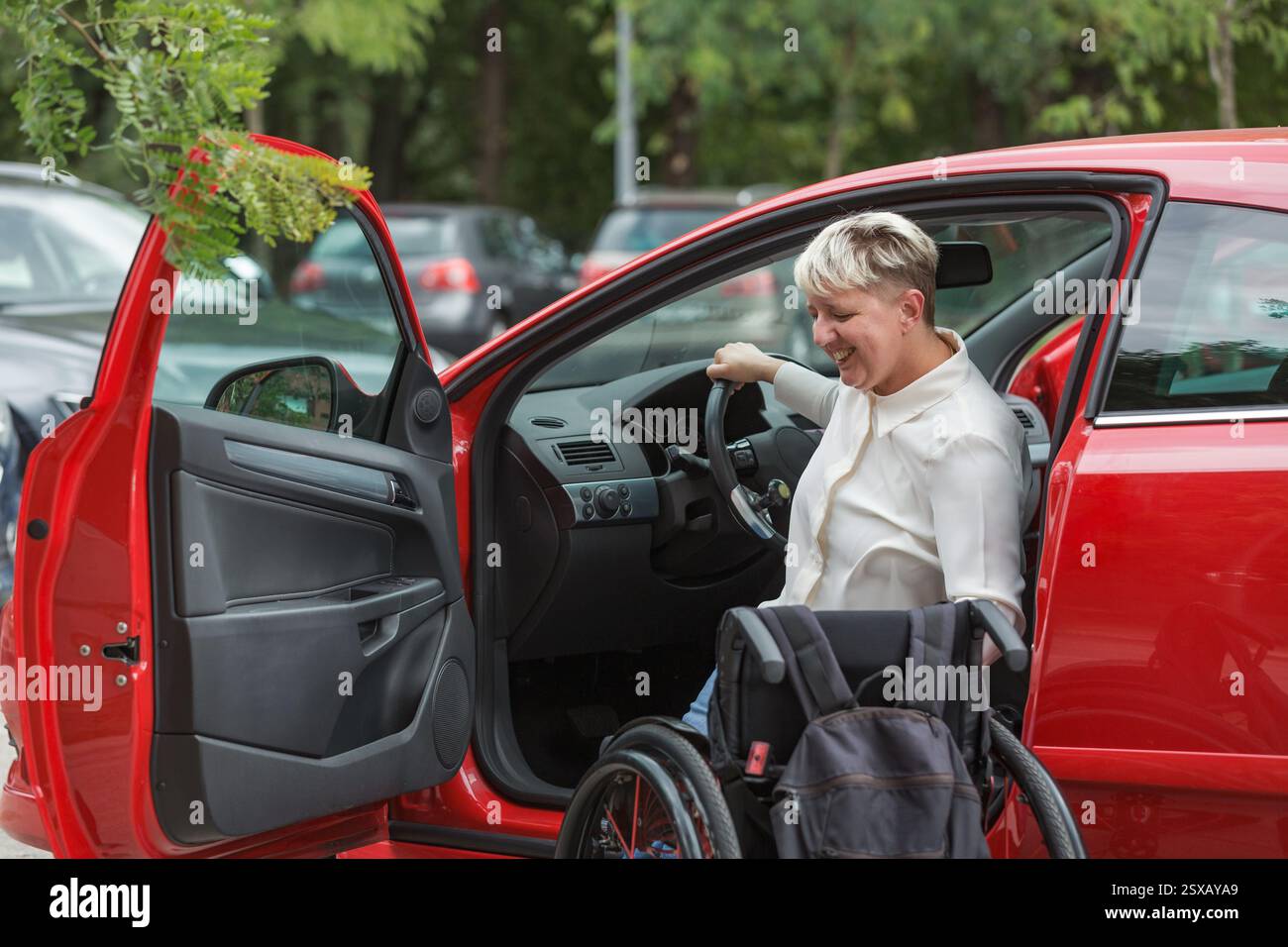 Eine behinderte Frau, die aus dem Auto steigt und vom Fahrersitz zum Rollstuhl wechselt. Unabhängiges Wohnkonzept. Stockfoto