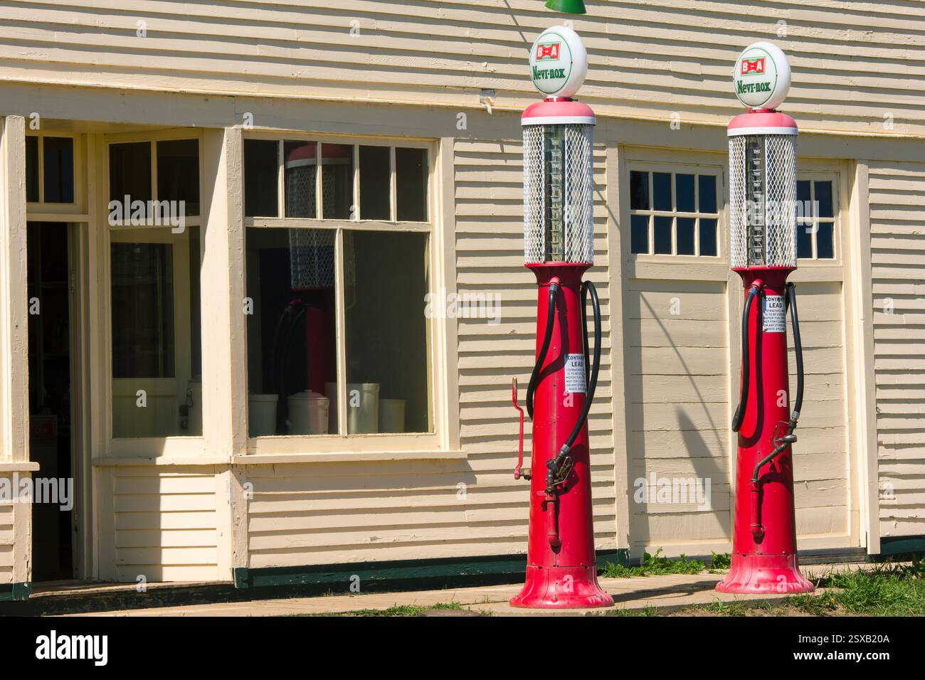 Zwei alte Gaspumpen befinden sich außerhalb eines Gebäudes. Eine der Pumpen ist rot und die andere weiß Stockfoto