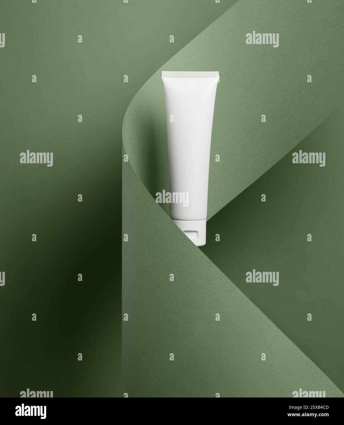 Ein minimalistisches, weißes Modell mit Kosmetikröhrchen wird elegant vor einem modernen grünen gefalteten Papierhintergrund präsentiert und sorgt für einen schicken und stilvollen Look Stockfoto