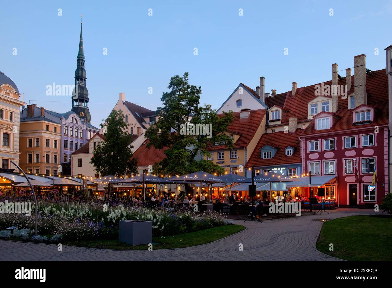 Ein malerischer Blick auf den Livu-Platz in der Altstadt von Riga, Lettland, mit farbenfrohen historischen Gebäuden, üppigem Grün und Cafés im Freien in einem beliebten Touristen Stockfoto