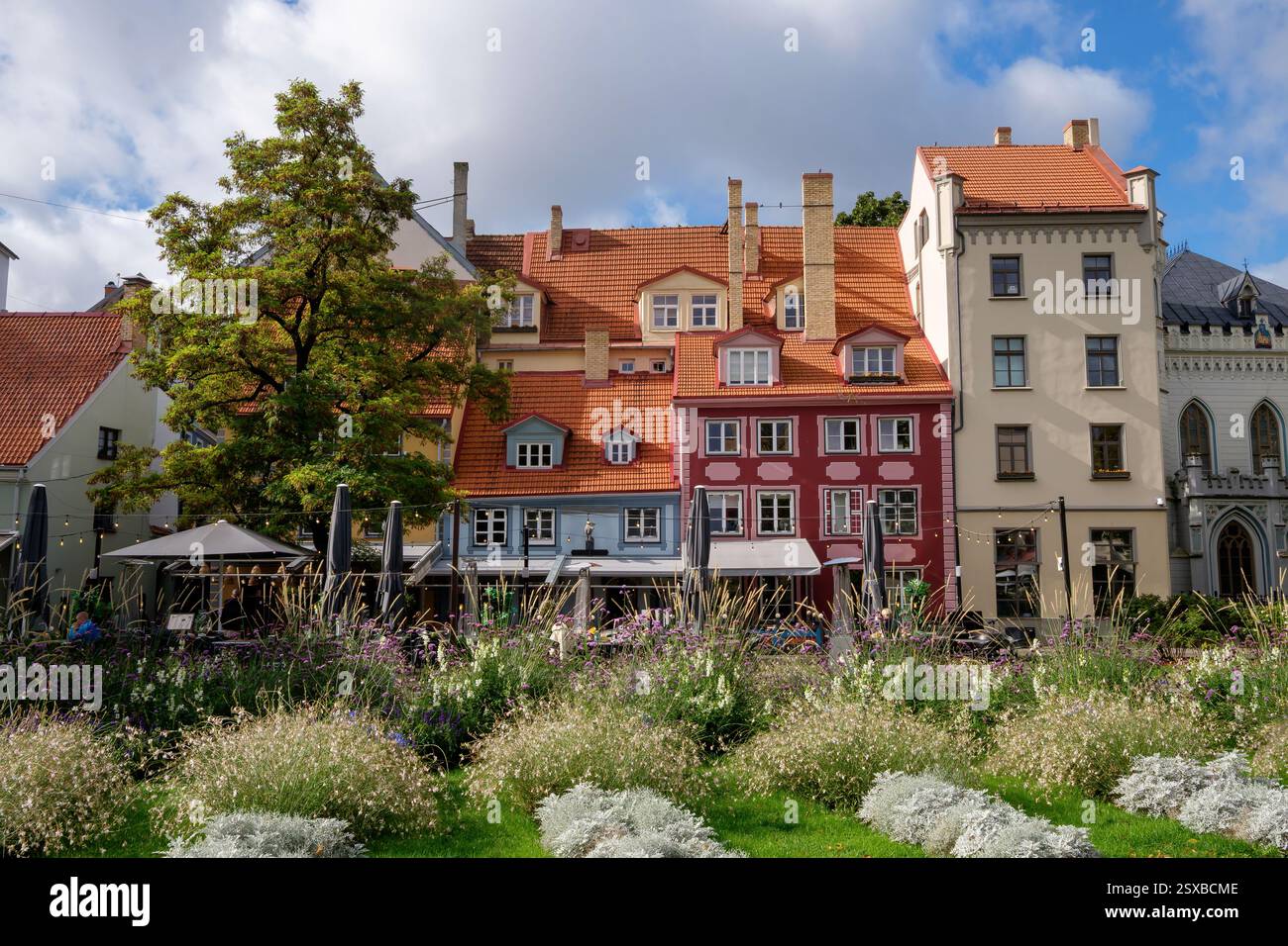 Ein malerischer Blick auf den Livu-Platz in der Altstadt von Riga, Lettland, mit farbenfrohen historischen Gebäuden, üppigem Grün und Cafés im Freien in einem beliebten Touristenviertel Stockfoto
